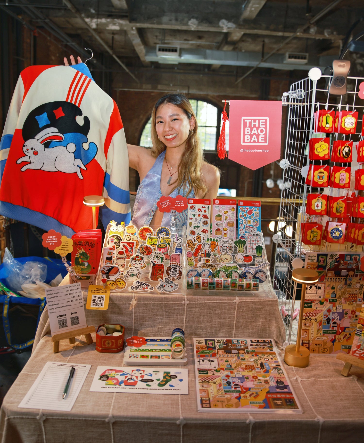 Christina standing behind a table with her artwork and holding up a white rabbit candy inspired jacket.