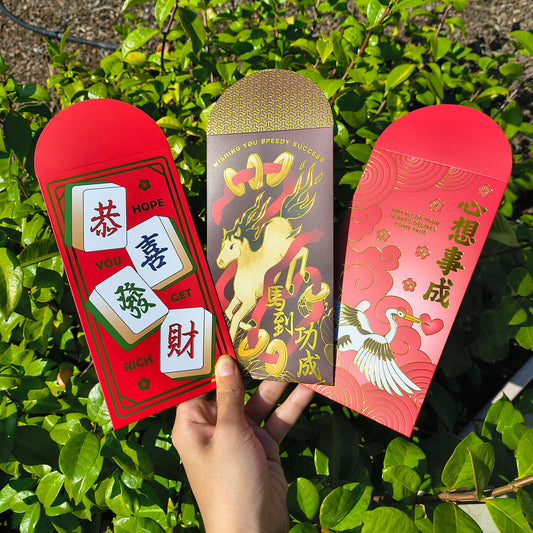 Three red envelopes with Chinese designs held by a hand against a green leafy background