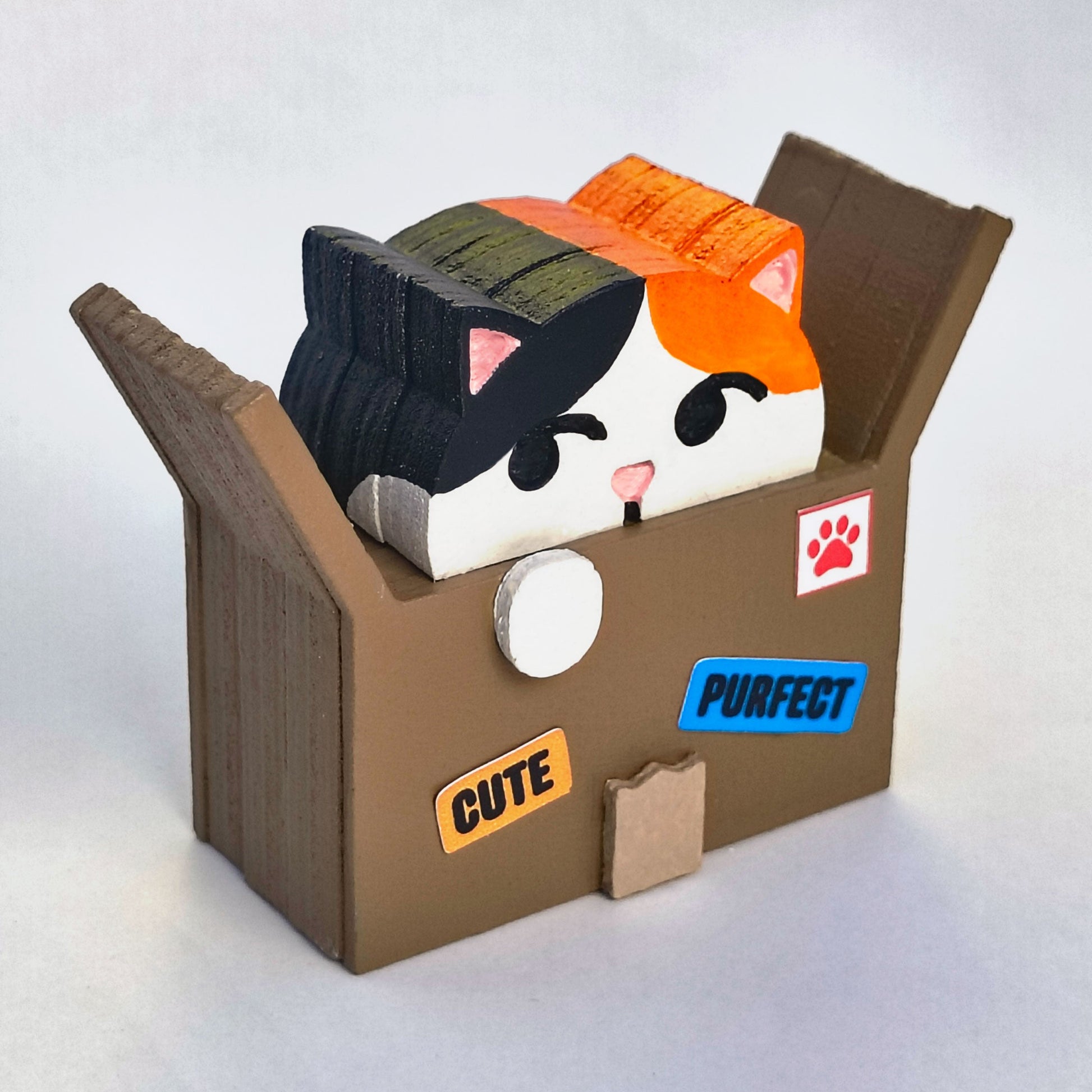 Wood figurine of a calico cat in a cardboard box with shipping label stickers that say "cute" and "purfect"