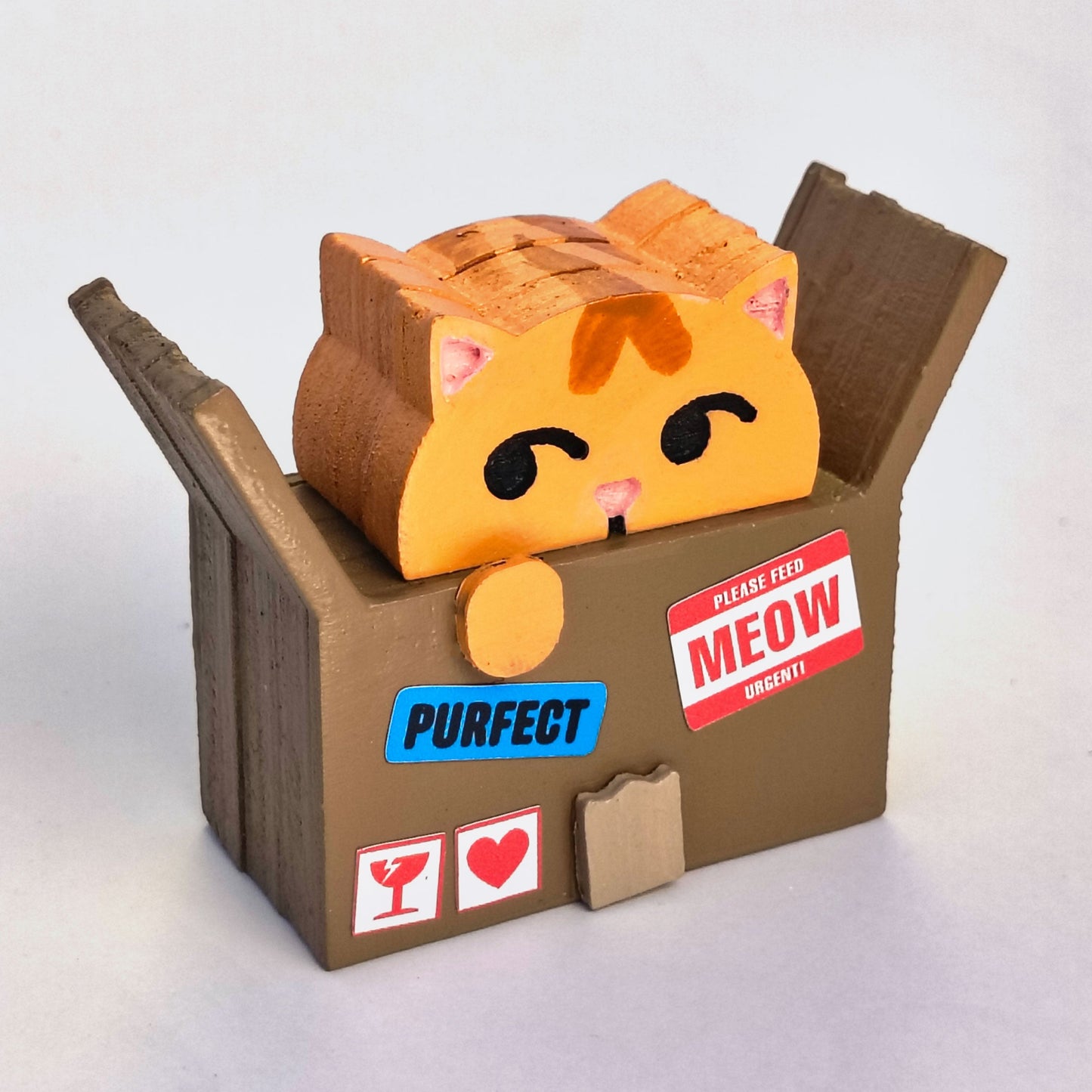 Wood figurine of an orange cat in a cardboard box with shipping label stickers that say "please feed meow urgent!" and "purfect"